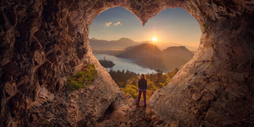 Young woman in heart shape cave towards the idyllic sunrise